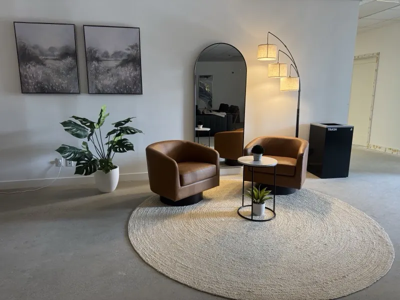 Waiting area with leather swivel chairs, round rug, and tall arched mirror